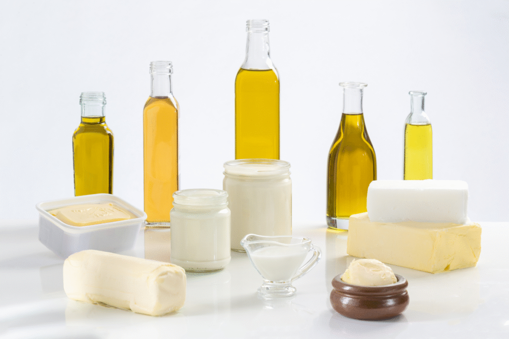 Assortment of high-calorie fats and oils including butter, cream, and olive oil bottles on a clean surface.